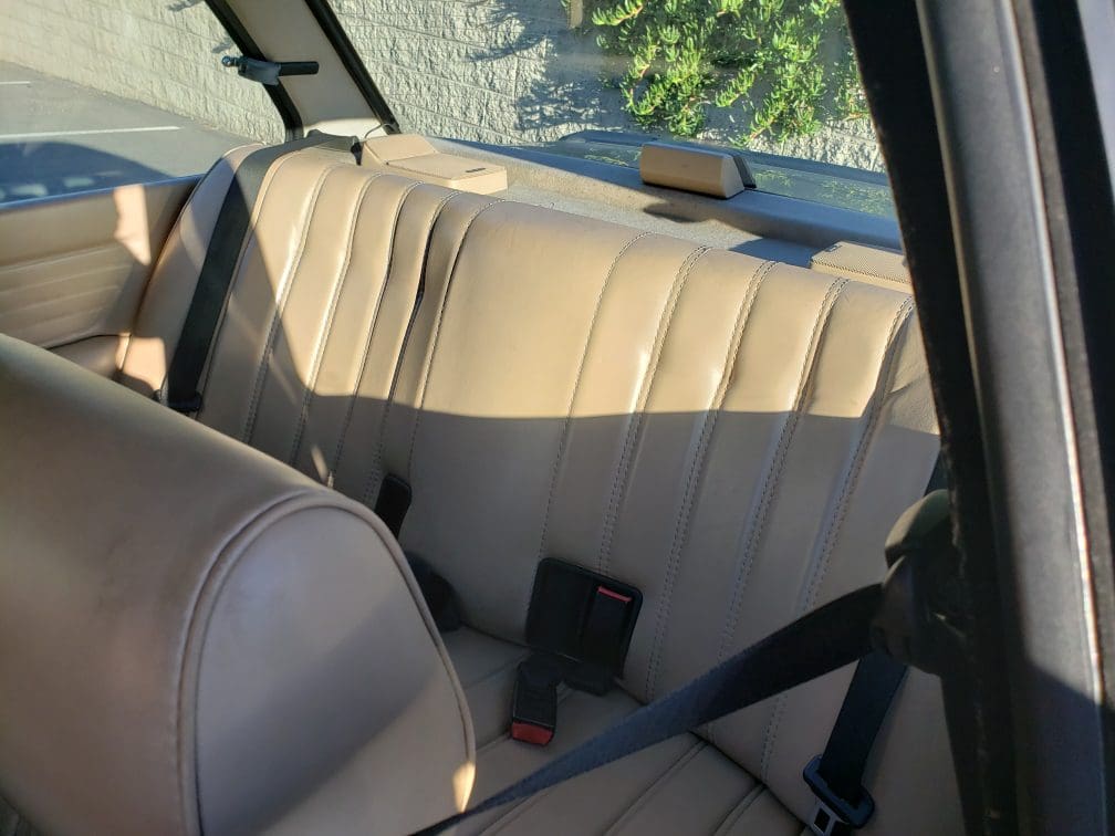 Backseat view of a car with beige leather seats and seatbelts.