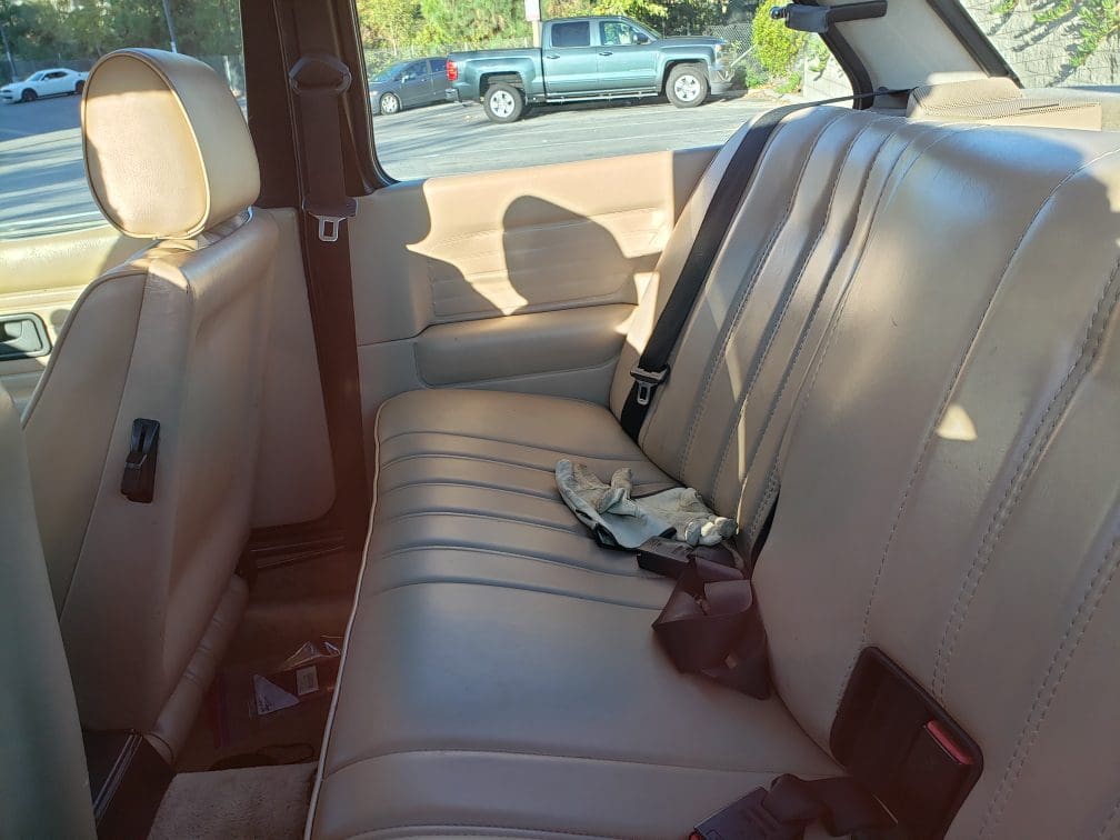 Clean beige leather car backseat with seatbelt and brown purse.