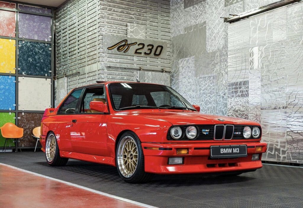 Classic red BMW E30 with gold rims parked indoors.