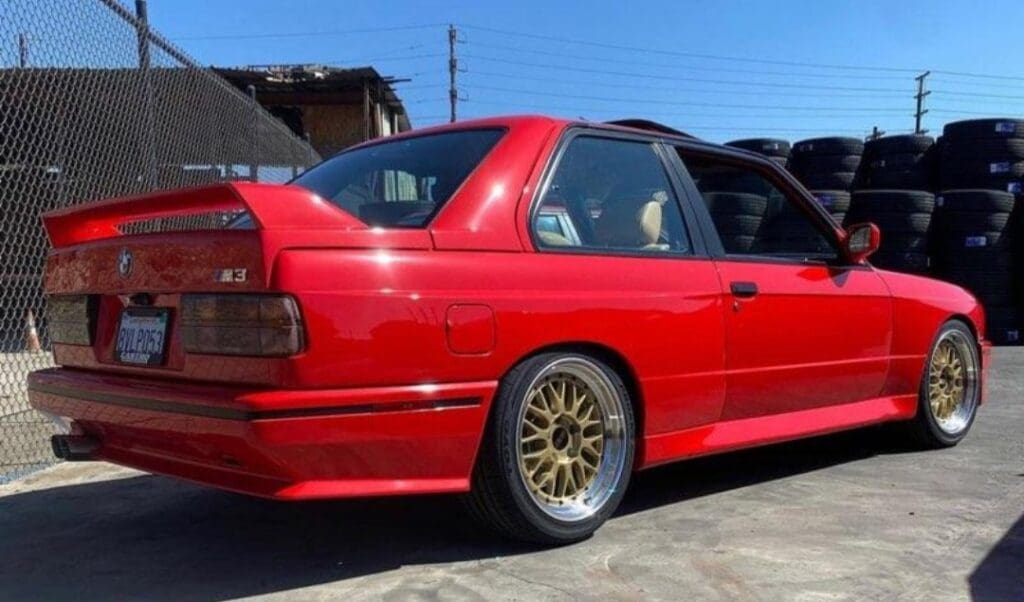 Red modified car with gold rims parked outdoors.