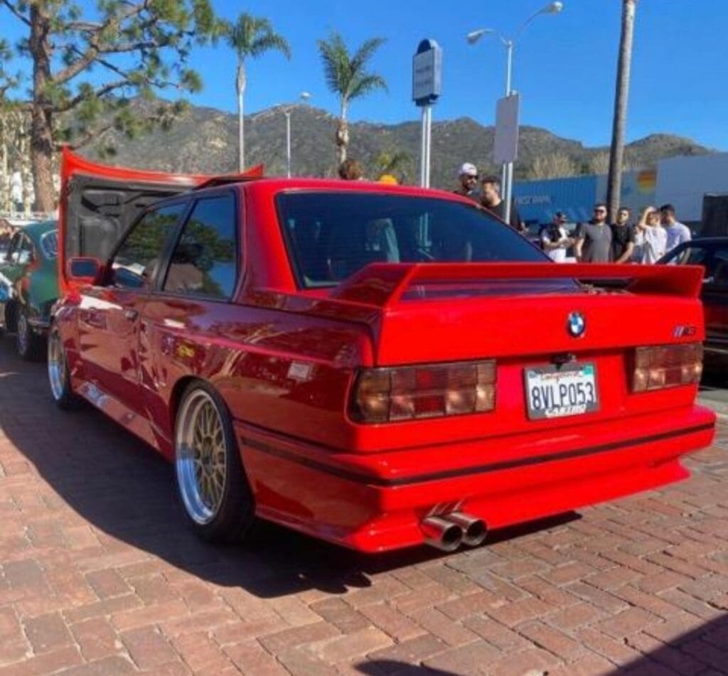 Red modified car with wide tires parked outdoors on a sunny day.