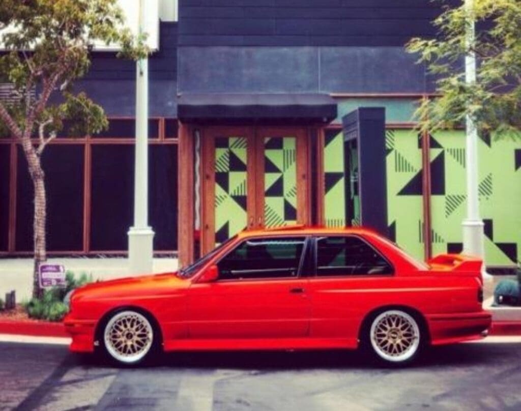 Red sports car parked beside a green building with geometric patterns.