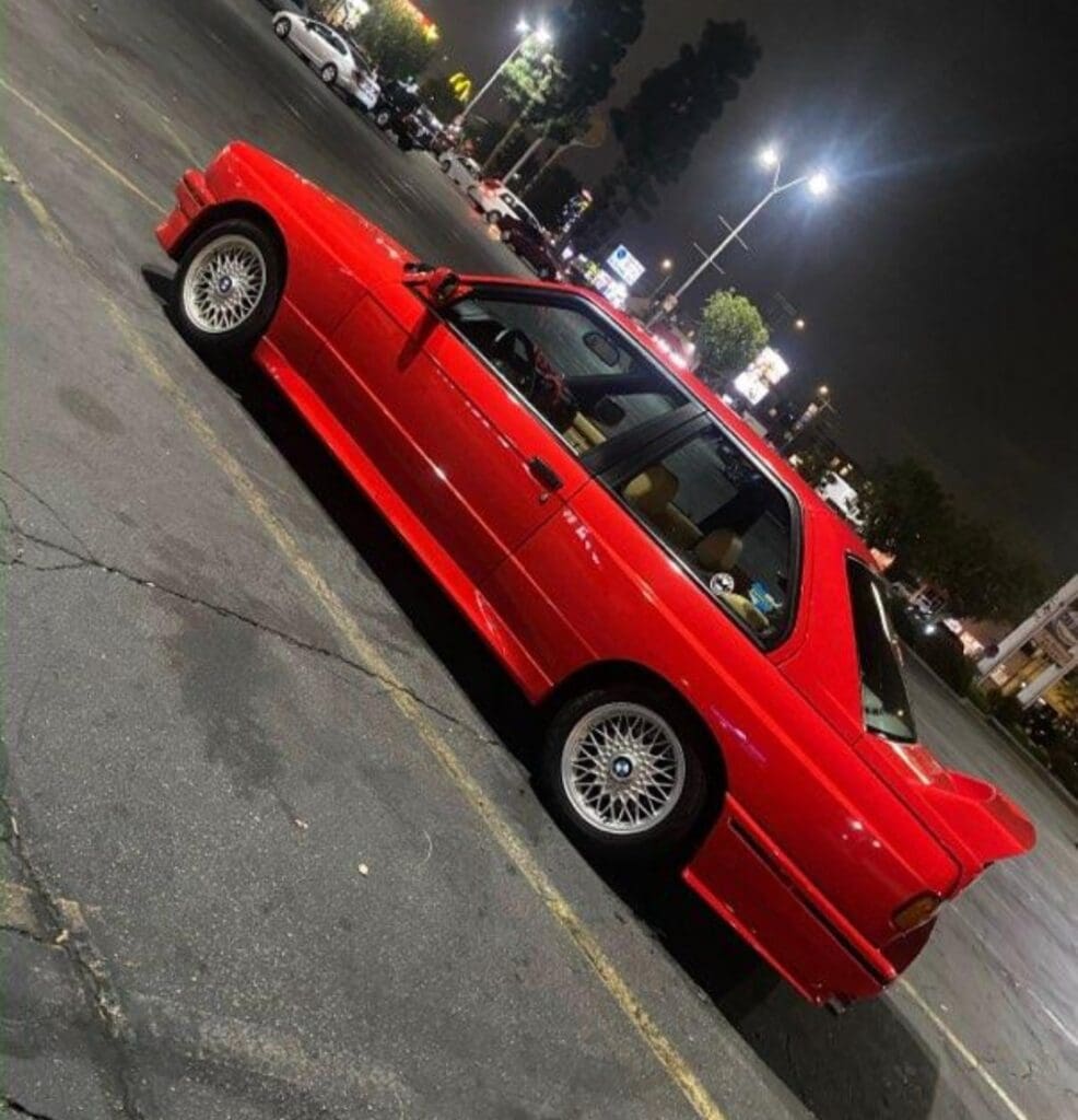 A red vintage car parked under streetlights at night.