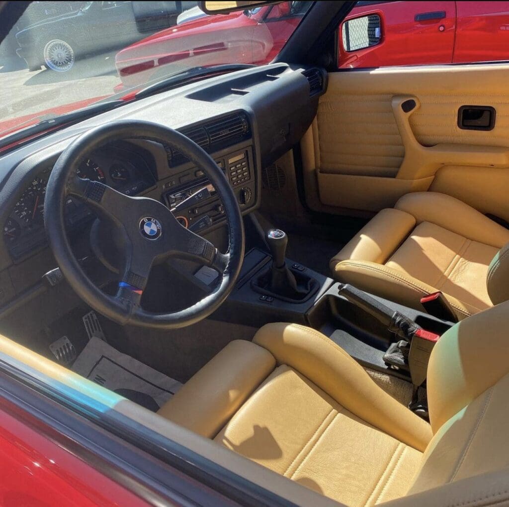 Interior of a vintage car with tan leather seats and a black steering wheel.
