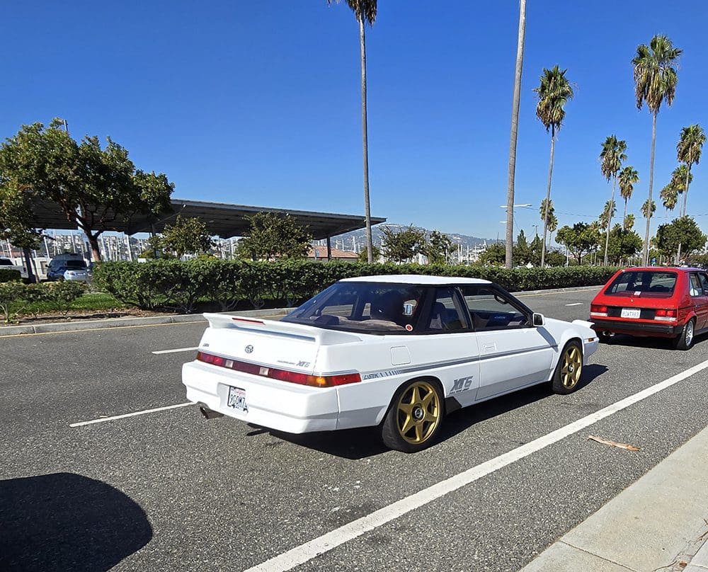 White vintage car with gold rims parked on a sunny street.