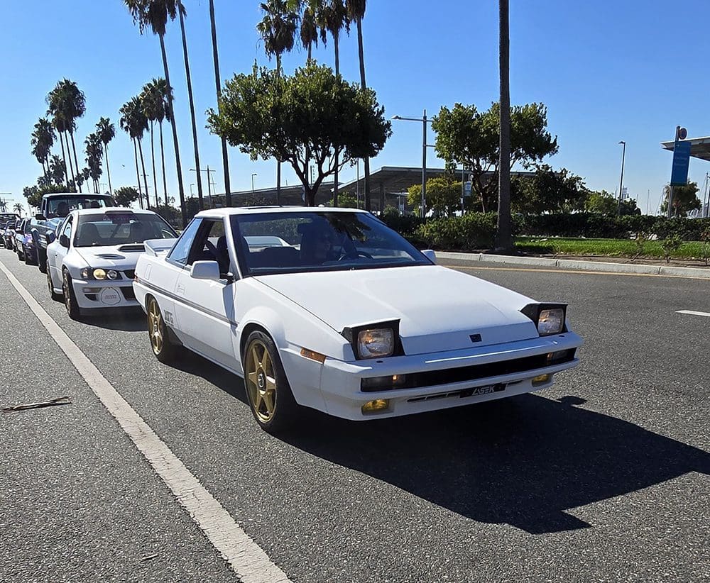 White vintage sports car parked by the roadside on a sunny day.