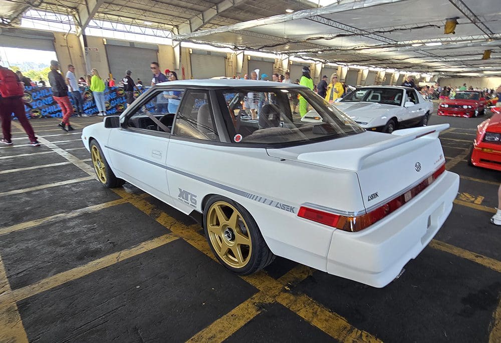 White classic coupe with gold wheels parked indoors.