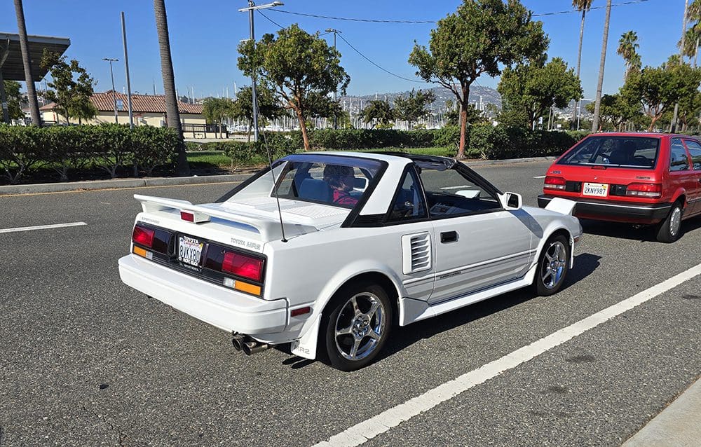 White convertible sports car with pop-up headlights in a sunny parking lot.