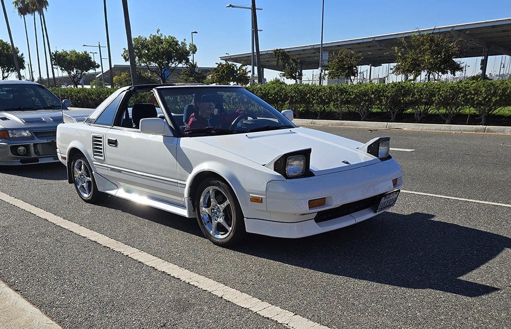 White vintage convertible car with pop-up headlights on a sunny day.