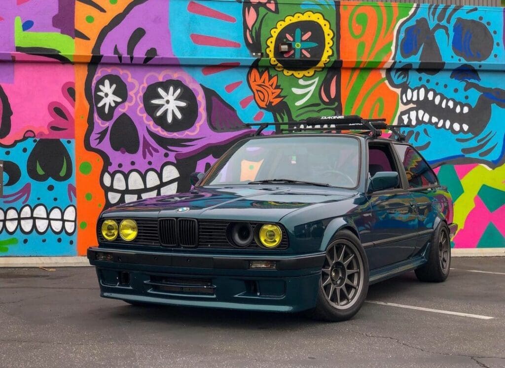 A black modified car parked in front of a colorful skull graffiti wall.
