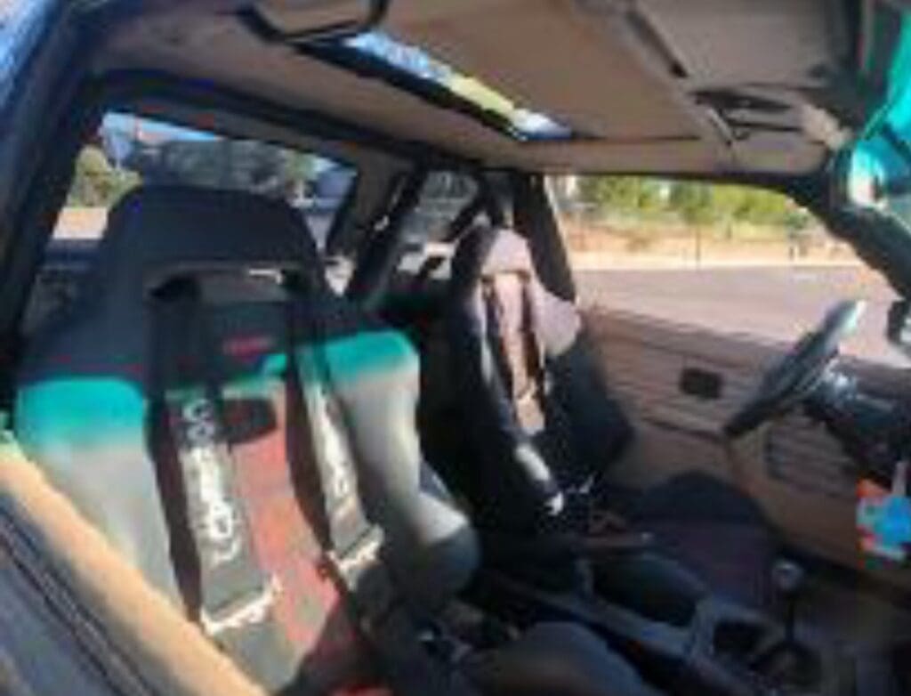 Interior of a car showing two black racing bucket seats with harnesses.