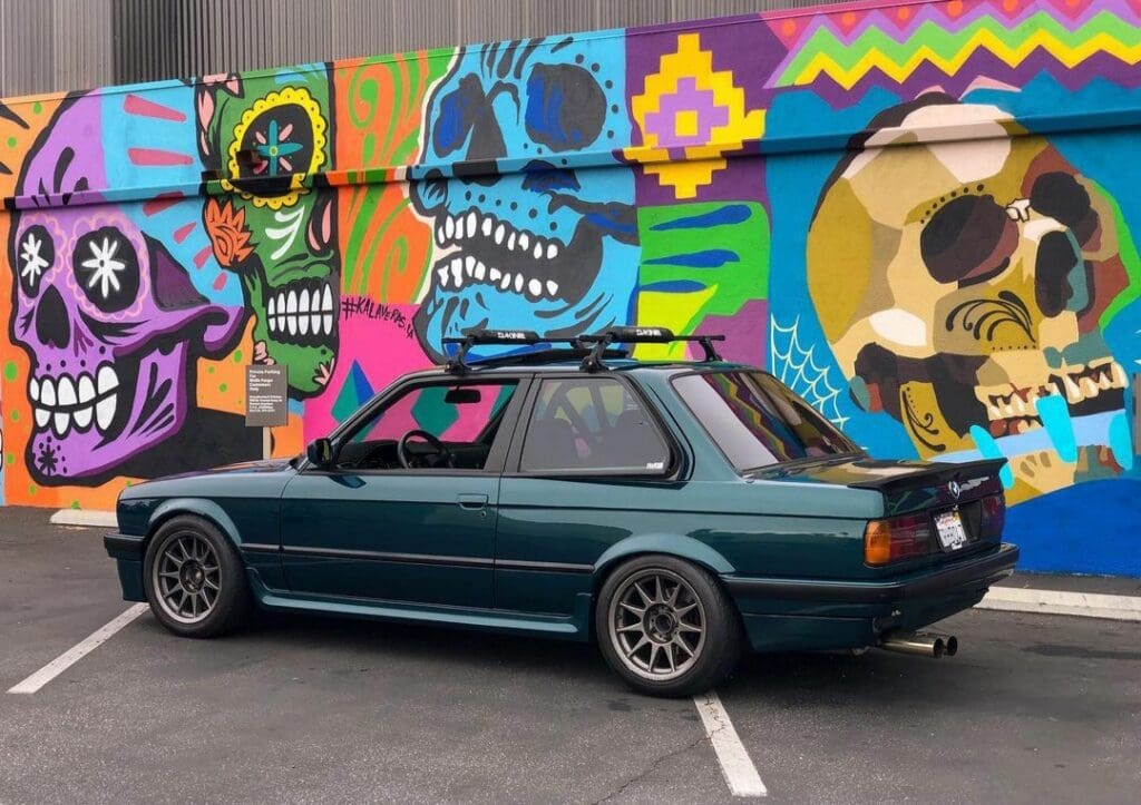 A classic car parked in front of a vibrant mural with colorful skull designs.