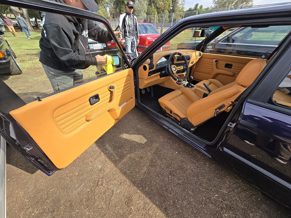 Classic black BMW convertible parked on grass with doors open.