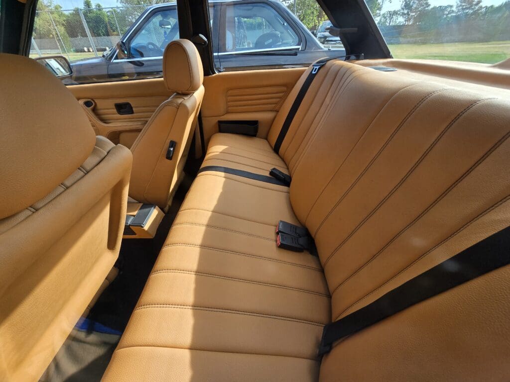 Classic black BMW convertible parked on grass with doors open.