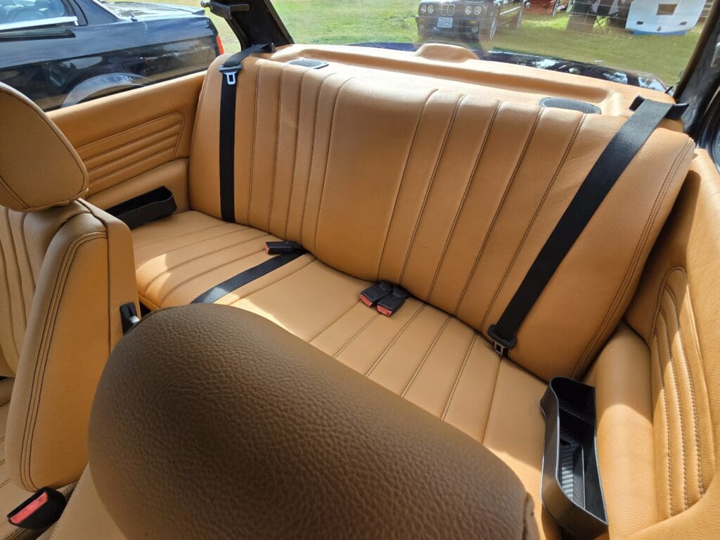 Classic black BMW convertible parked on grass with doors open.