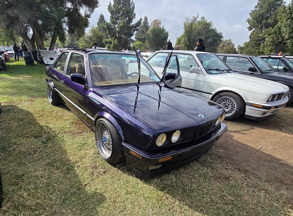 Classic black BMW with windshield wipers raised, parked on grass at a car show.