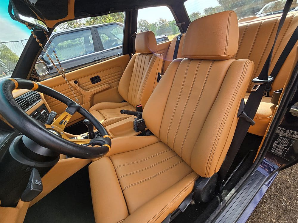 Classic car interior with tan leather seats and wooden steering wheel.