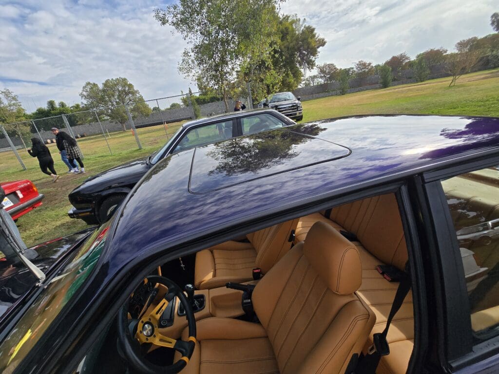 Interior view of a vintage car with tan leather seats and a wooden steering wheel.