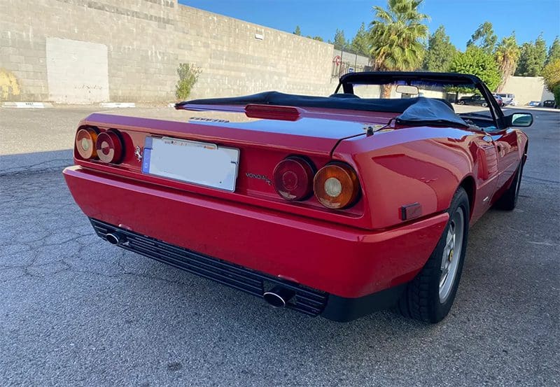 Red classic sports car parked outdoors with dual exhausts.