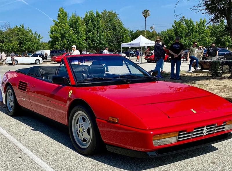 Red convertible Ferrari sports car parked outdoors on a sunny day.