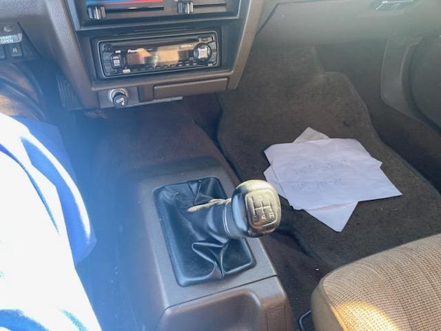 Manual gear shift inside a car with a paper on the passenger seat.