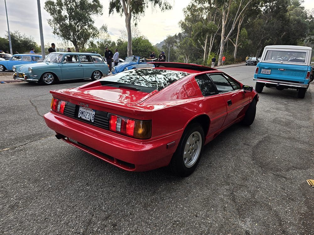Red sports car parked on a roadside with trees in the background.