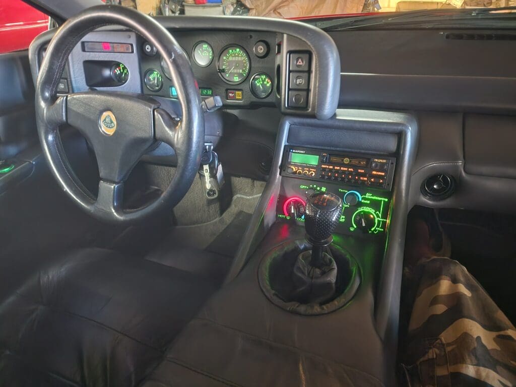 Car interior showing steering wheel, dashboard, and gear shift with colorful knobs.