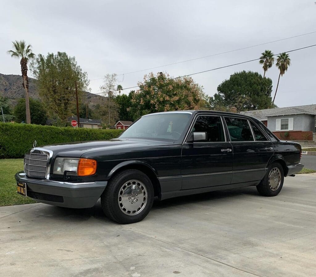 Classic black limousine parked on a driveway under cloudy skies.