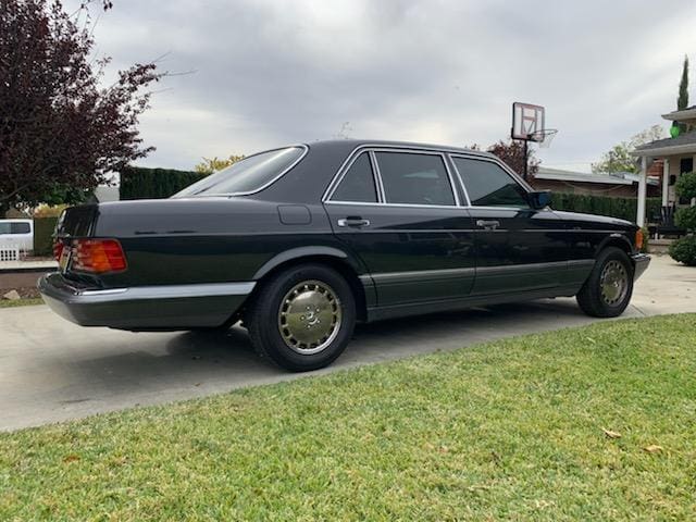 Classic black luxury sedan parked on a driveway beside a grassy lawn.