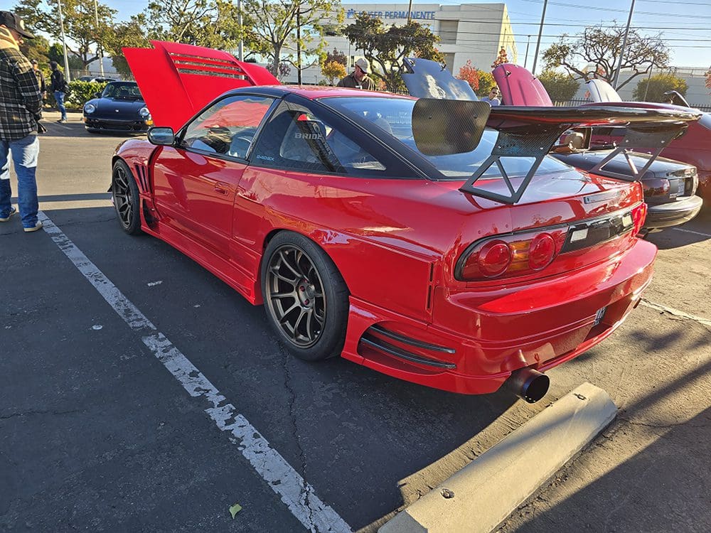 Red sports car with aftermarket wheels and a large rear spoiler in a parking lot.