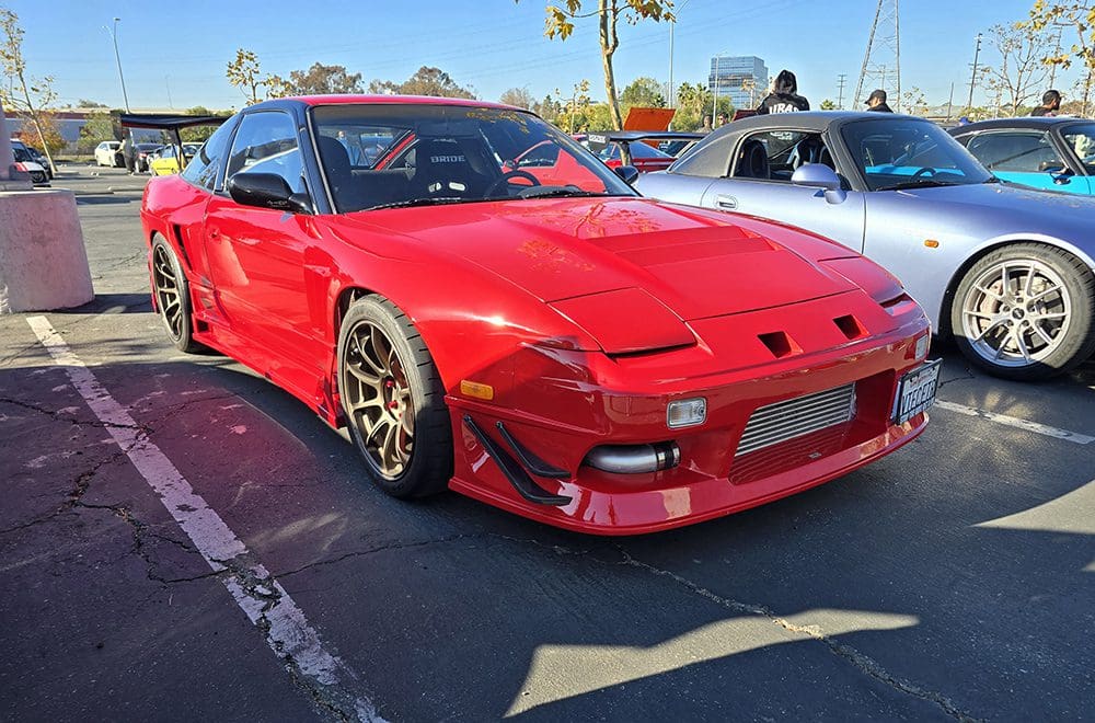 Red sports car with custom wheels parked in a lot on a sunny day.