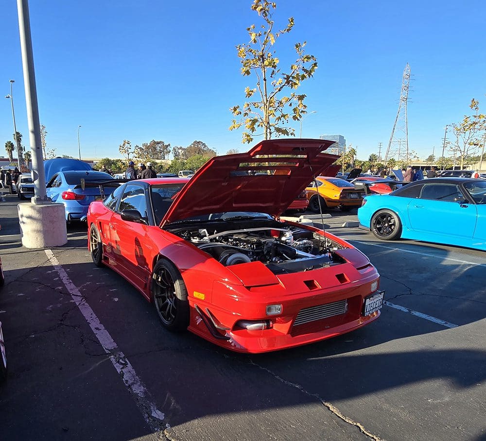 Red sports car with its hood open at a car show.