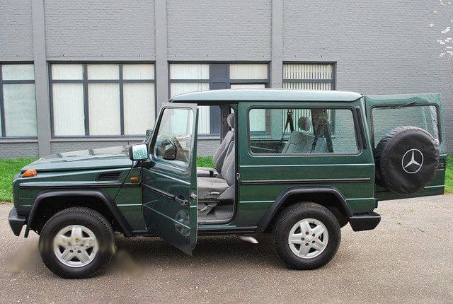 Green SUV with open door parked near a building.