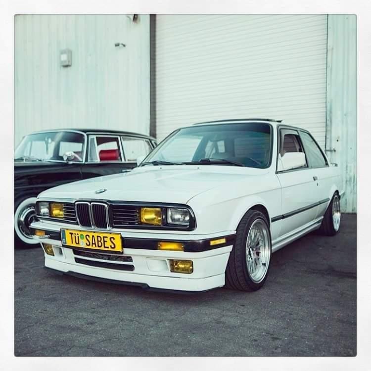 Classic white BMW E30 parked indoors with a vintage aesthetic.