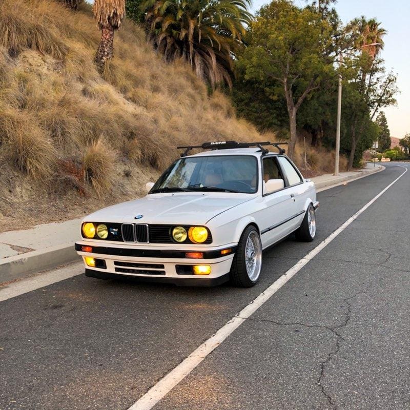 Classic white BMW E30 parked on a quiet street at dusk.