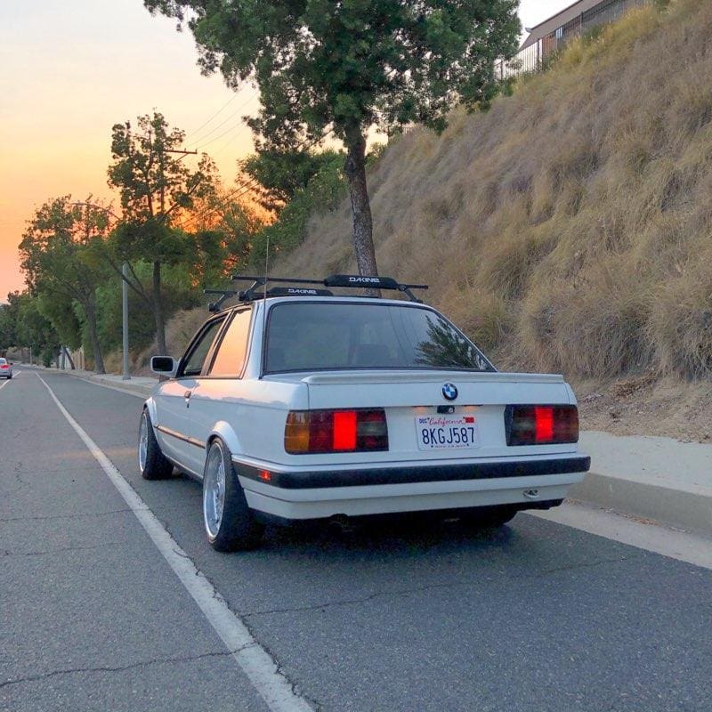 Classic white BMW E30 with roof rack parked on a roadside.