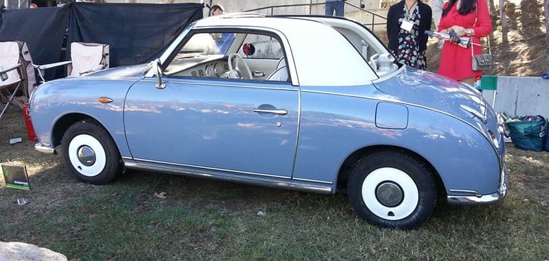 A vintage blue convertible car parked on grass with a white roof.