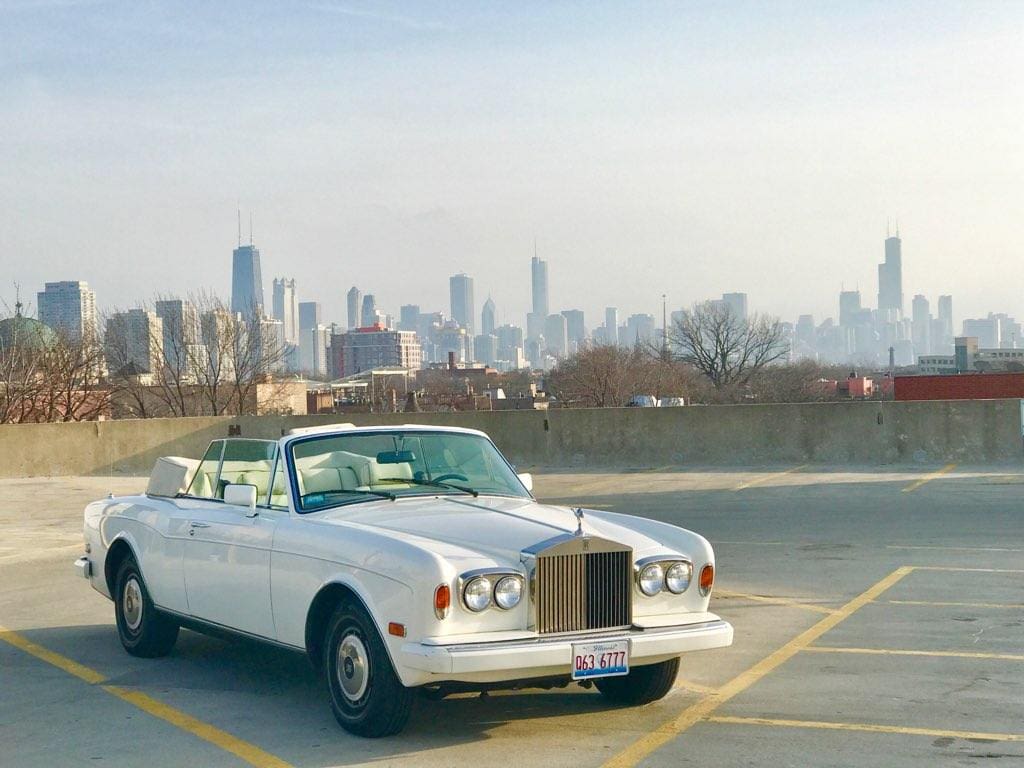 A classic white Rolls-Royce parked with a city skyline in the background.