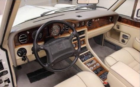 Classic car interior with wooden dashboard and beige leather seats.