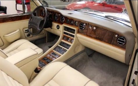Luxurious car interior with beige leather and wood trim.
