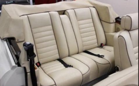 Cream leather car backseat with seat belts and stitching details.