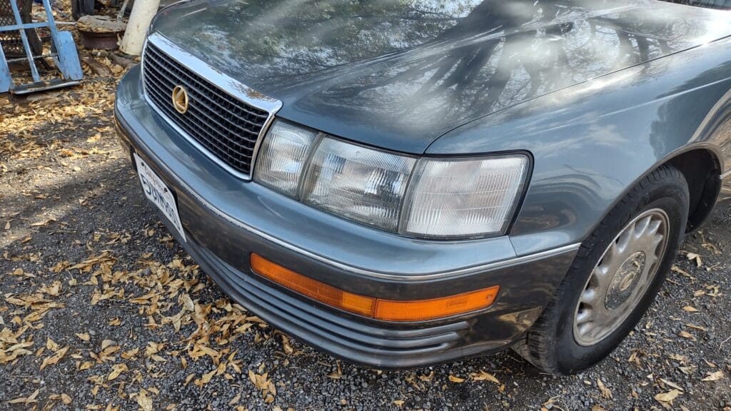 Close-up of a vintage car's front headlight and grille with orange indicator lights.