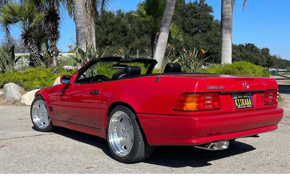 Red convertible sports car parked near palm trees on a sunny day.