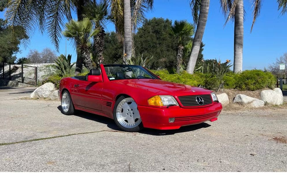 Red convertible sports car parked by palm trees under a clear blue sky.