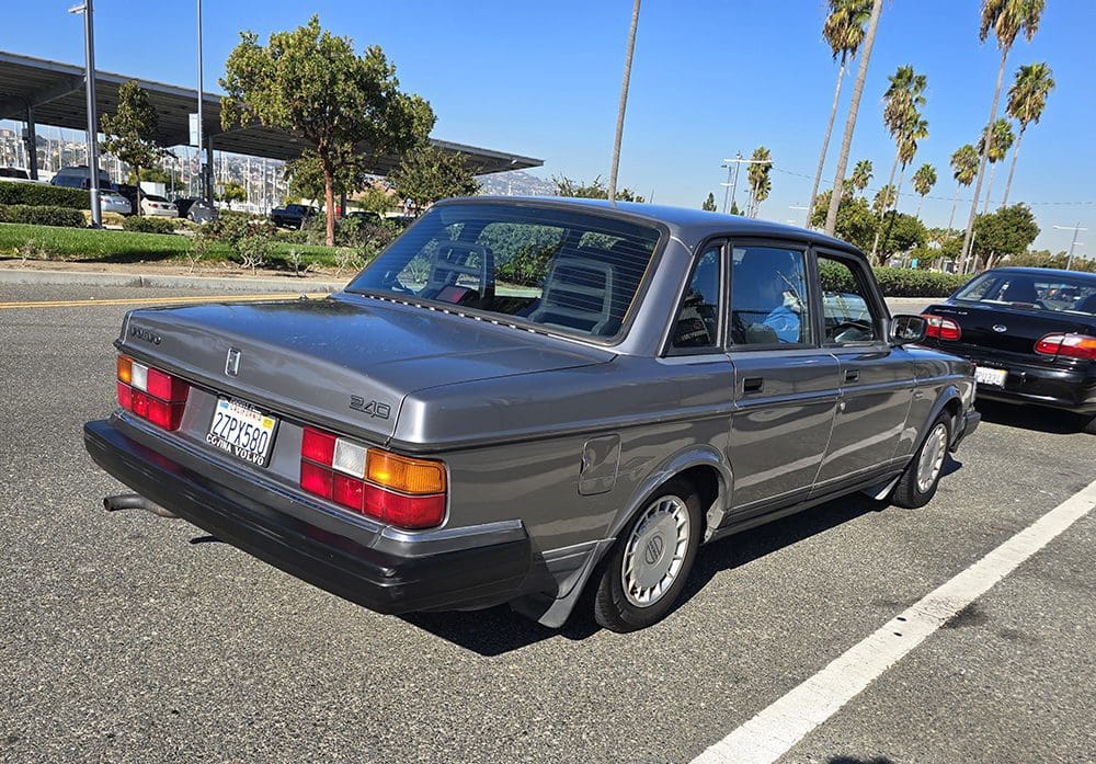 Classic gray Volvo sedan parked in a sunny lot with palm trees.