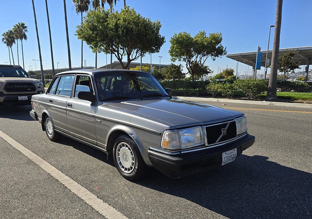 Classic silver Volvo sedan parked on a sunny street with palm trees.