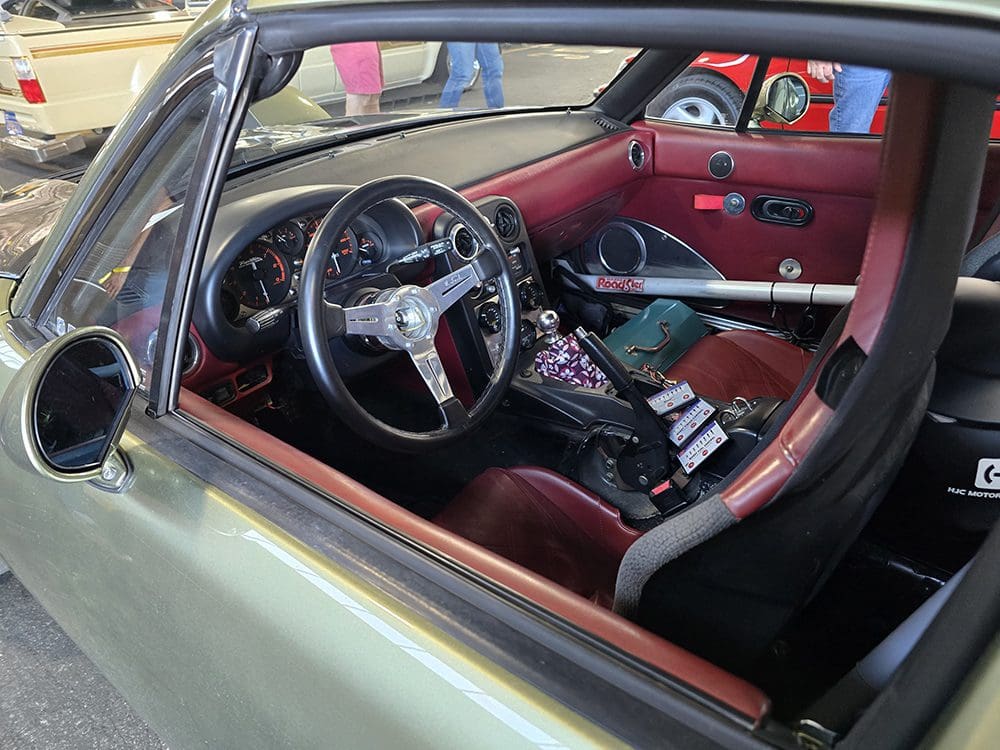 Interior of a classic car featuring a vintage steering wheel and red leather seats.