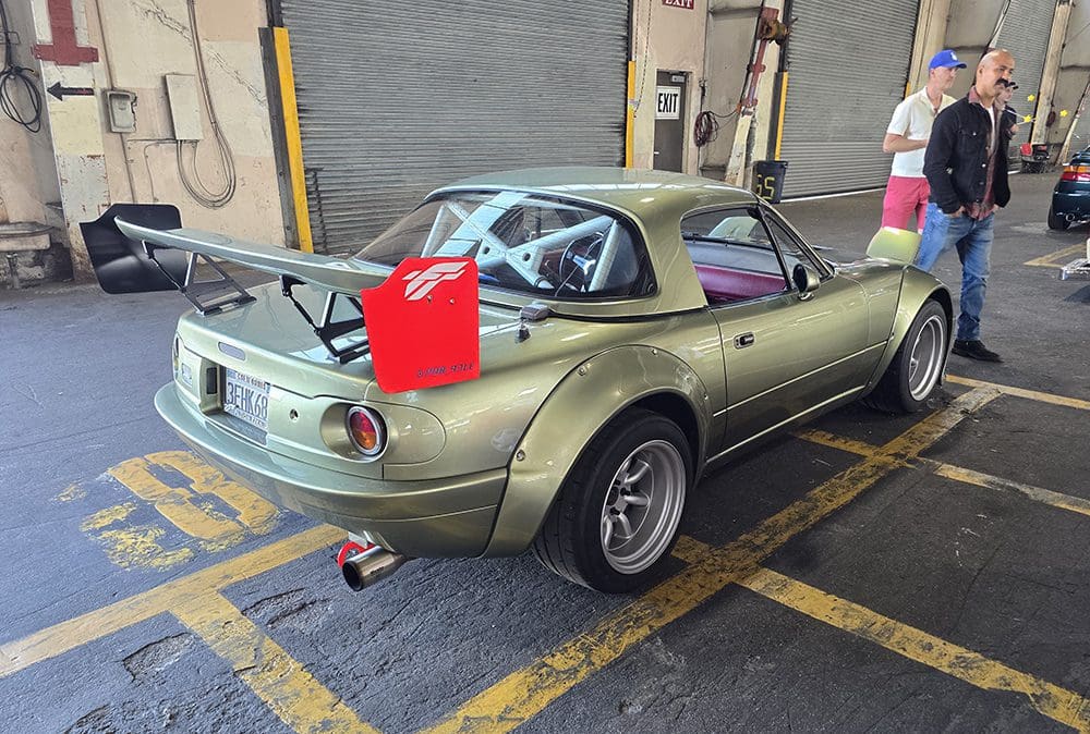 Modified green convertible car with a red fuel canister on the rear wing.