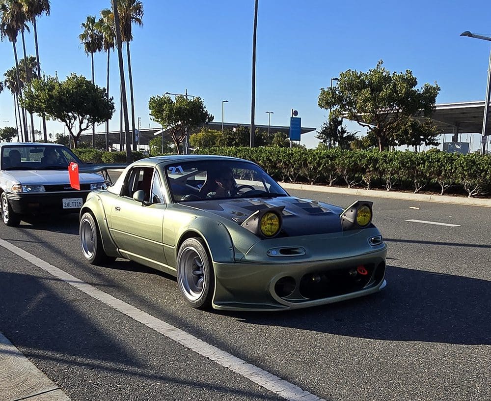 Modified green sports car with pop-up headlights on a sunny street.