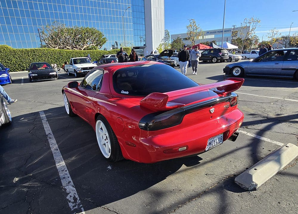Red sports car with large rear spoiler parked outdoors on a sunny day.